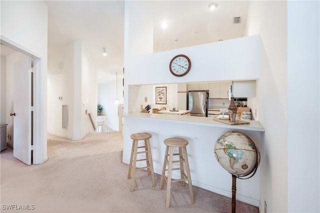 kitchen with white cabinetry, kitchen peninsula, light carpet, and stainless steel fridge