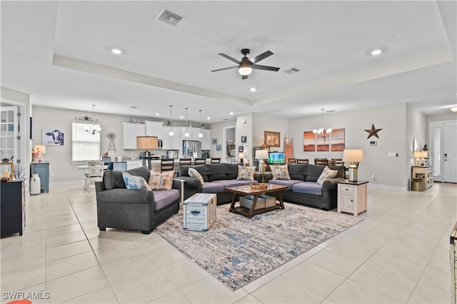 tiled living room with ceiling fan with notable chandelier and a raised ceiling