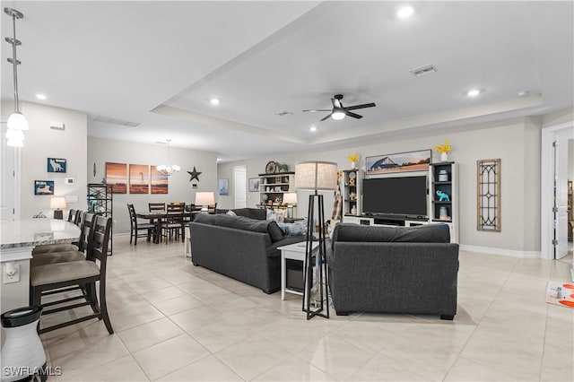 living room with light tile patterned floors, a tray ceiling, and ceiling fan with notable chandelier