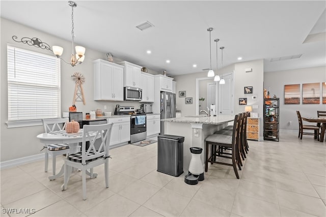 kitchen featuring light stone countertops, appliances with stainless steel finishes, an island with sink, white cabinetry, and decorative light fixtures