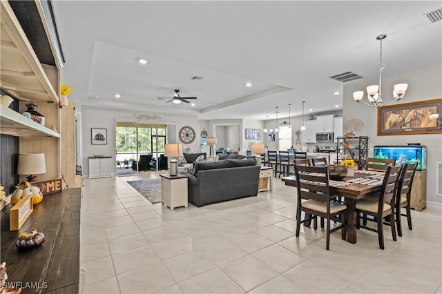 dining room with light tile patterned flooring, ceiling fan with notable chandelier, and a raised ceiling