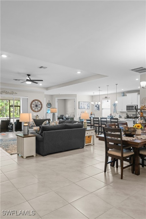 tiled living room featuring ceiling fan with notable chandelier and a raised ceiling