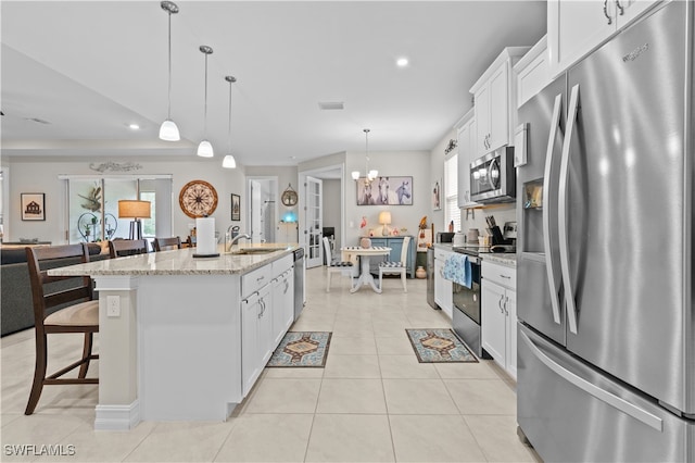 kitchen featuring appliances with stainless steel finishes, white cabinets, light stone counters, and an island with sink