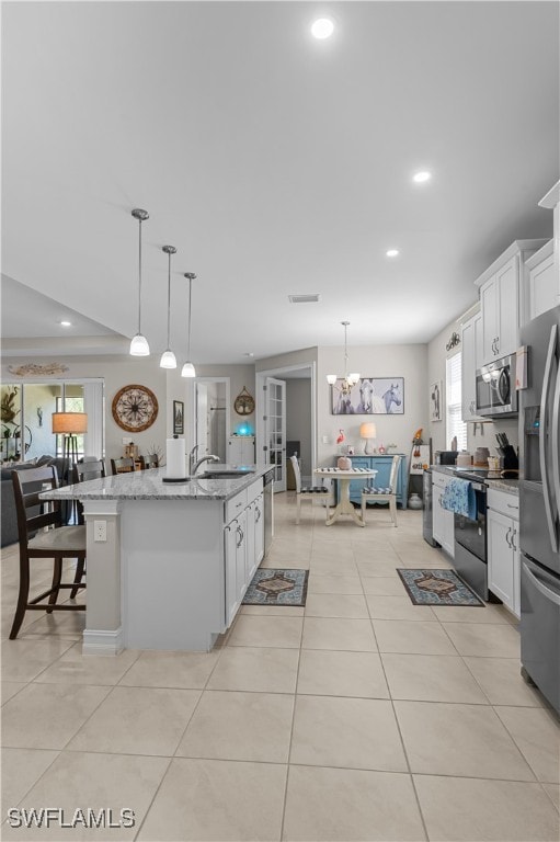 kitchen with white cabinets, stainless steel appliances, pendant lighting, and a kitchen island with sink