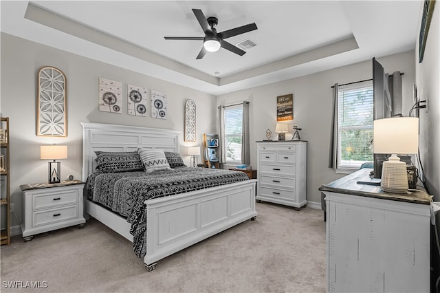 bedroom with multiple windows, ceiling fan, light colored carpet, and a raised ceiling