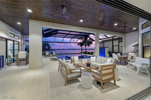 patio terrace at dusk with glass enclosure, ceiling fan, a water view, and an outdoor hangout area