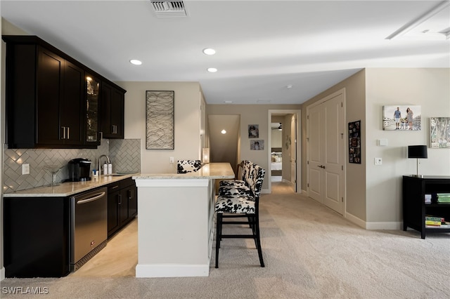 kitchen with light stone countertops, a kitchen breakfast bar, light carpet, stainless steel dishwasher, and a kitchen island