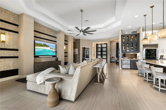 living room featuring a raised ceiling, ceiling fan, and light tile patterned flooring