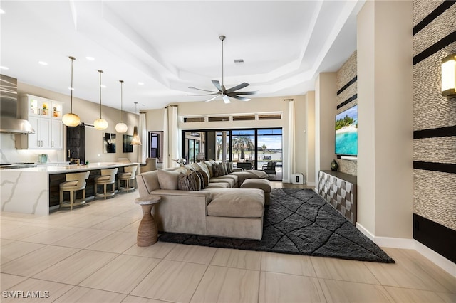 living room featuring light tile patterned floors, a raised ceiling, and ceiling fan