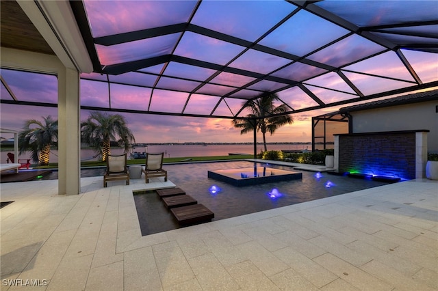 pool at dusk with a water view, pool water feature, a lanai, an in ground hot tub, and a patio area