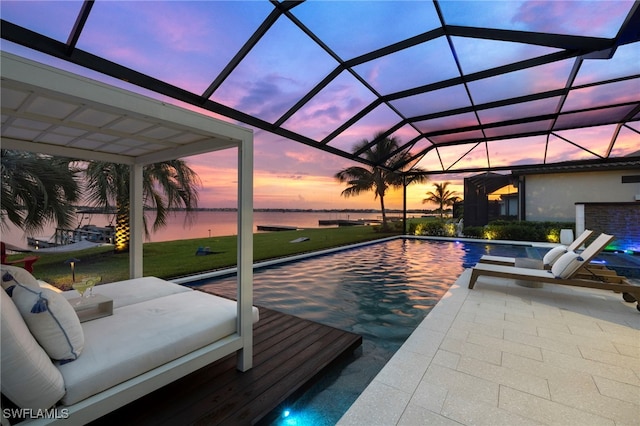 pool at dusk with a lanai, a water view, a yard, and a patio