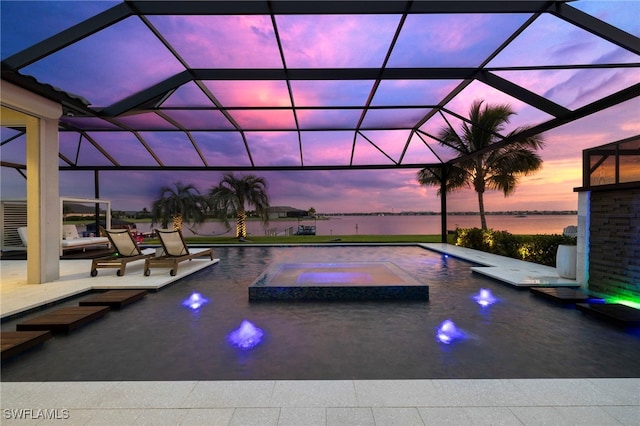 pool at dusk featuring an in ground hot tub, a patio, a water view, and glass enclosure