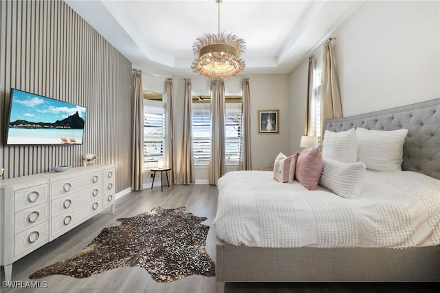 bedroom featuring a raised ceiling, wood-type flooring, and an inviting chandelier