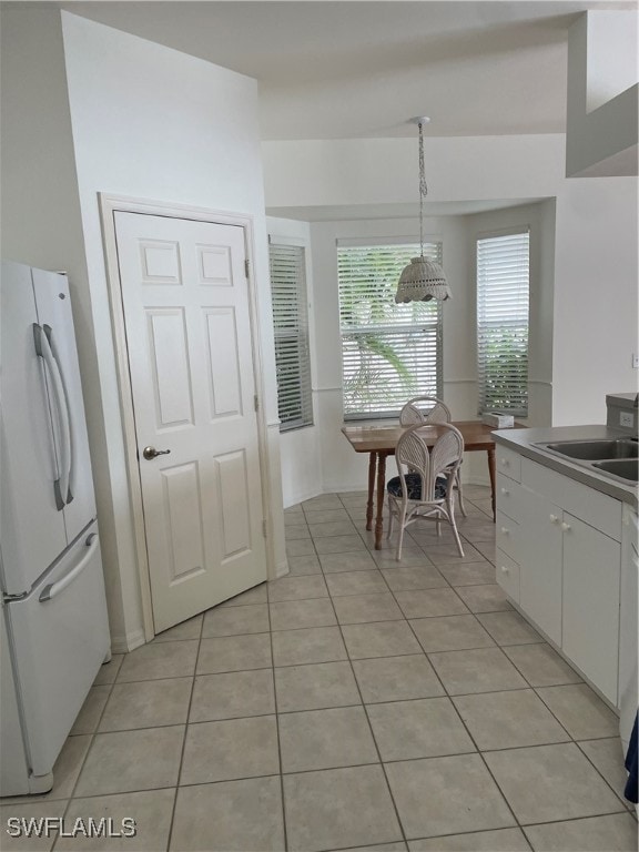 kitchen with light tile patterned flooring, white cabinetry, white refrigerator, hanging light fixtures, and sink