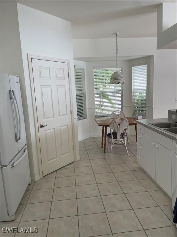 592 Crossfield Cir, Naples, FL 34104 - kitchen with freestanding refrigerator, light tile patterned floors, white cabinetry, a sink, and pendant lighting
