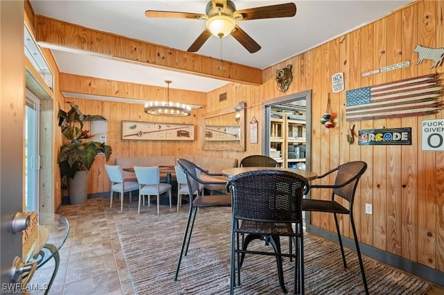 dining space featuring wooden walls and ceiling fan with notable chandelier