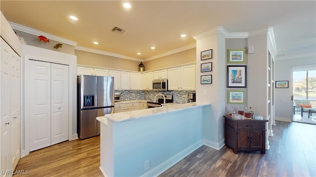 kitchen featuring crown molding, appliances with stainless steel finishes, white cabinets, dark wood-type flooring, and kitchen peninsula