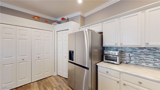 kitchen with tasteful backsplash, ornamental molding, stainless steel fridge, light wood-type flooring, and white cabinets