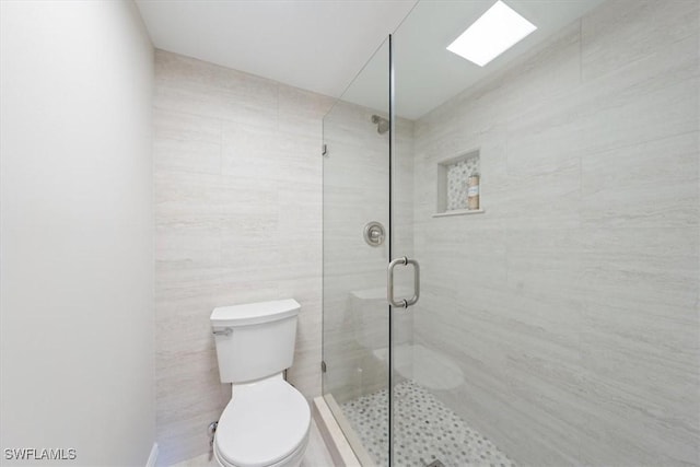 bathroom with toilet, a shower with shower door, and tile walls