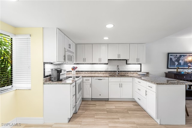 kitchen featuring dark stone counters, white cabinetry, kitchen peninsula, sink, and white appliances