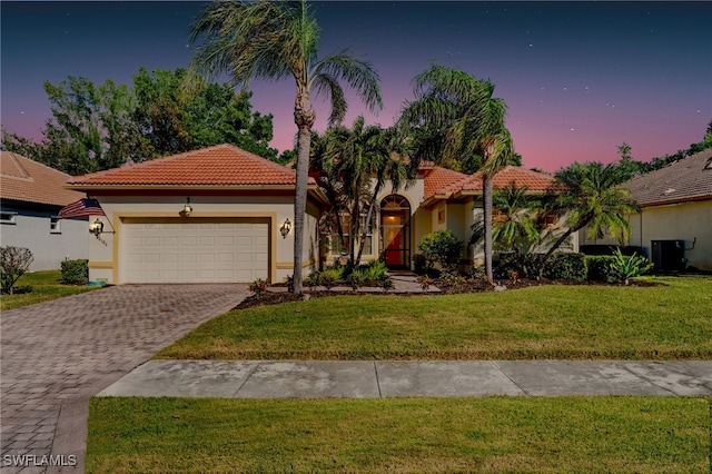 view of front of home with a yard, central AC unit, and a garage