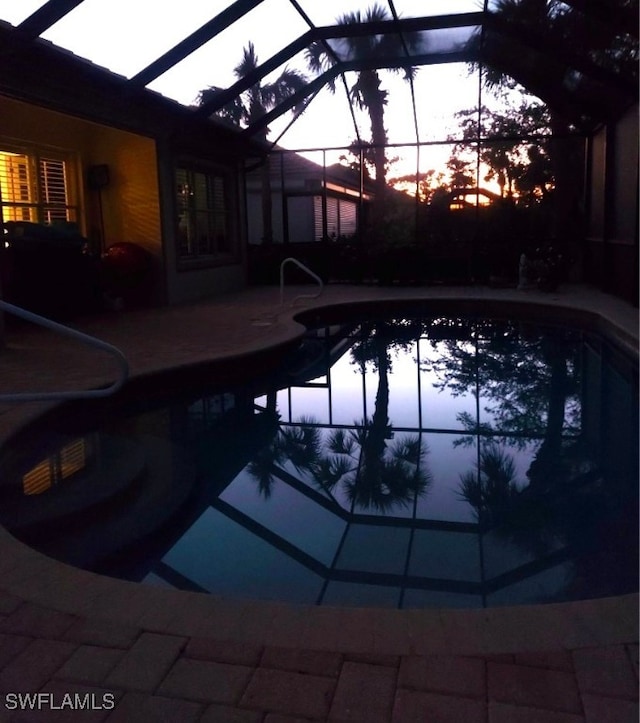 pool at dusk with a patio and glass enclosure