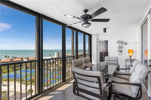 sunroom with ceiling fan and a water view