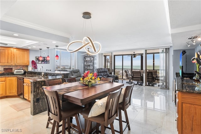 dining area with crown molding, a notable chandelier, a raised ceiling, expansive windows, and sink