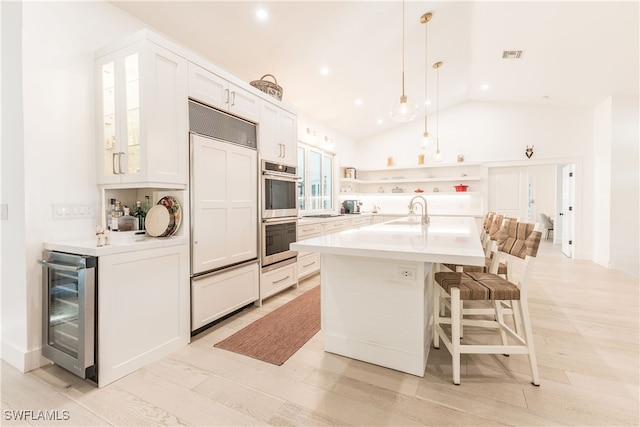 kitchen featuring lofted ceiling, pendant lighting, white cabinetry, an island with sink, and beverage cooler