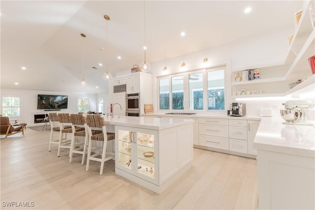 kitchen featuring white cabinetry, light hardwood / wood-style floors, decorative light fixtures, a kitchen breakfast bar, and a large island with sink