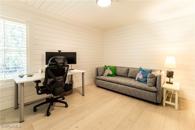 home office with plenty of natural light, light hardwood / wood-style flooring, and wood walls