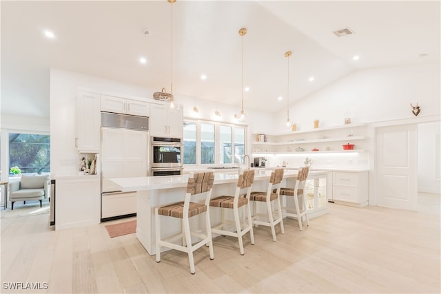 kitchen featuring vaulted ceiling, paneled fridge, hanging light fixtures, a kitchen island with sink, and white cabinets