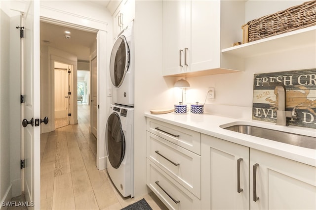 clothes washing area with cabinets, stacked washer and dryer, sink, and light hardwood / wood-style flooring