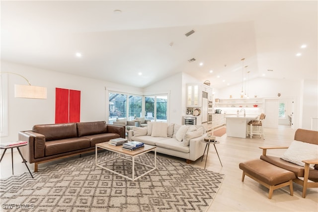 living room featuring light hardwood / wood-style floors, high vaulted ceiling, and sink