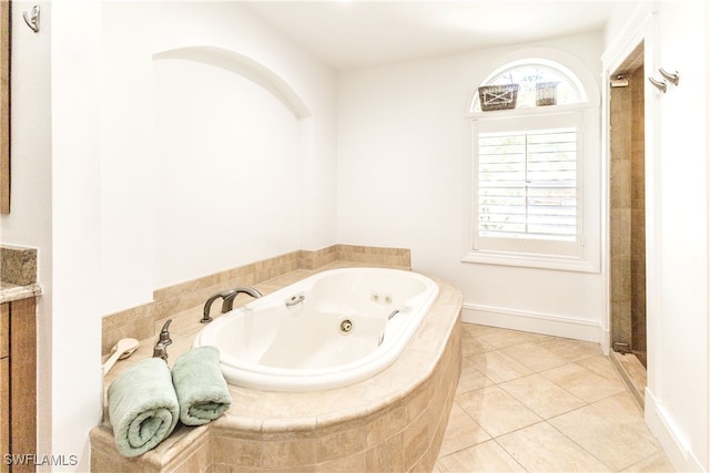 bathroom featuring a relaxing tiled tub, vanity, and tile patterned flooring