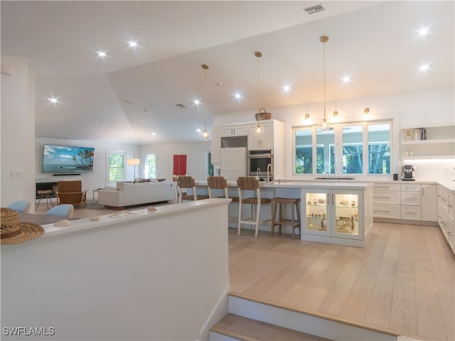 kitchen featuring decorative light fixtures, vaulted ceiling, white cabinetry, light wood-type flooring, and a kitchen breakfast bar