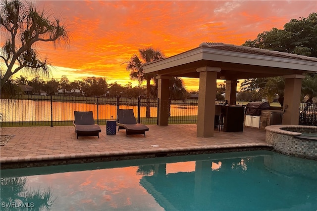 pool at dusk with a gazebo, a patio area, an in ground hot tub, and grilling area