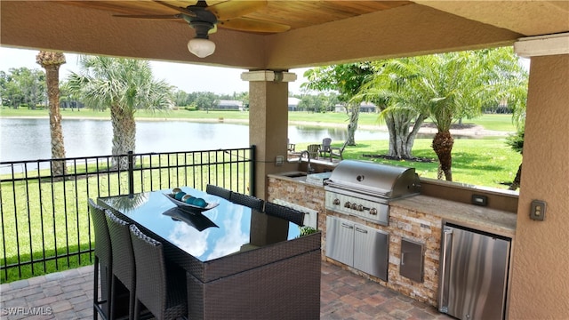 view of patio featuring a water view, ceiling fan, area for grilling, and an outdoor kitchen