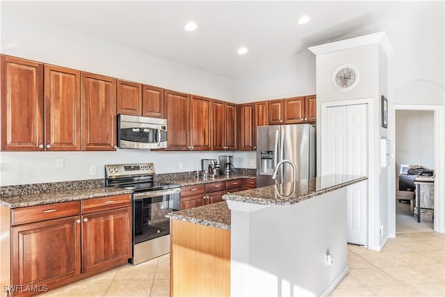 kitchen with a center island with sink, light tile patterned floors, appliances with stainless steel finishes, and dark stone counters