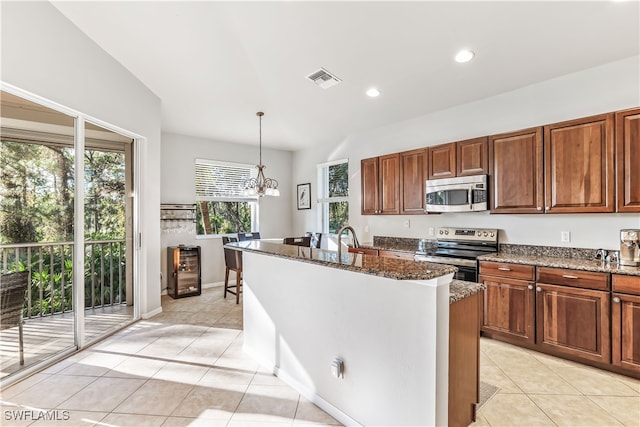 kitchen featuring appliances with stainless steel finishes, decorative light fixtures, an inviting chandelier, dark stone countertops, and an island with sink