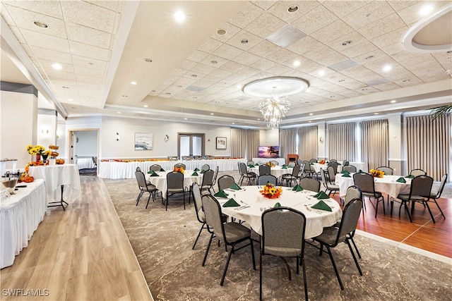 dining space with a drop ceiling, a raised ceiling, and light wood-type flooring