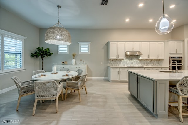 kitchen with decorative backsplash, white cabinets, hanging light fixtures, and stainless steel double oven