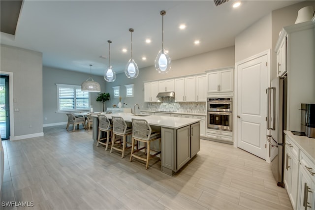 kitchen with stainless steel appliances, a center island with sink, pendant lighting, white cabinetry, and tasteful backsplash