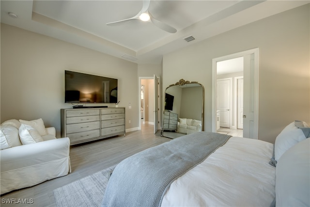 bedroom featuring ensuite bathroom, a tray ceiling, light wood-type flooring, and ceiling fan