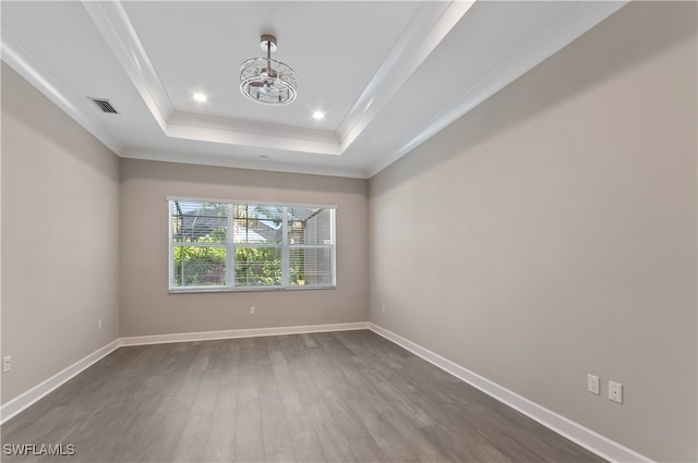 empty room with wood-type flooring, a raised ceiling, ornamental molding, and a notable chandelier