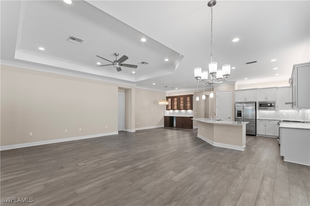 kitchen with a tray ceiling, a kitchen island with sink, pendant lighting, and stainless steel appliances