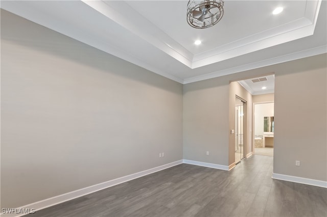 spare room featuring a raised ceiling, crown molding, and dark wood-type flooring