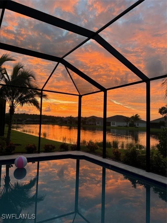 pool at dusk featuring a water view and a lanai