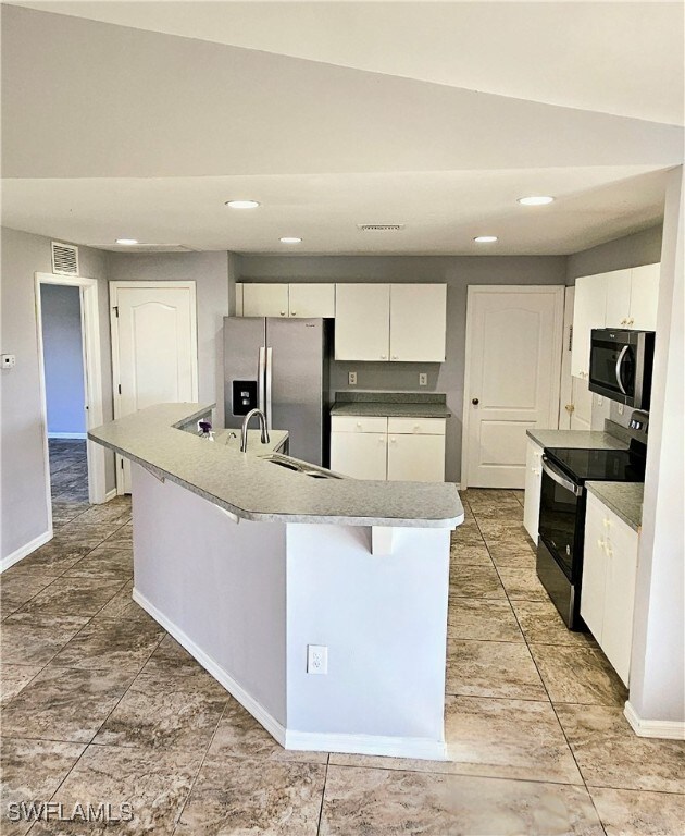 kitchen featuring appliances with stainless steel finishes, sink, vaulted ceiling, white cabinets, and a kitchen island with sink