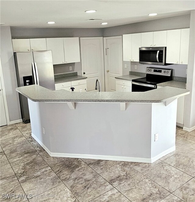 kitchen featuring white cabinets, appliances with stainless steel finishes, a kitchen breakfast bar, and a kitchen island with sink